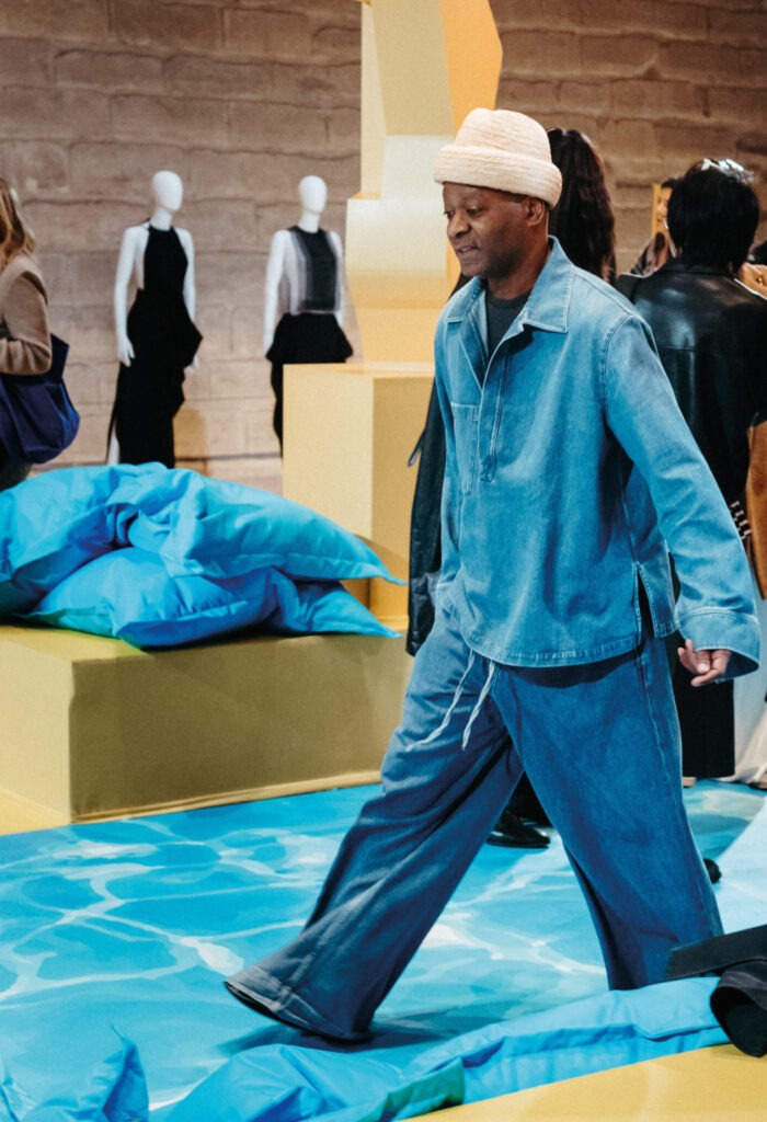 Homme qui défile vêtu d'un ensemble en denim dans un lieu et une ambiance de défilé jaune et bleu
